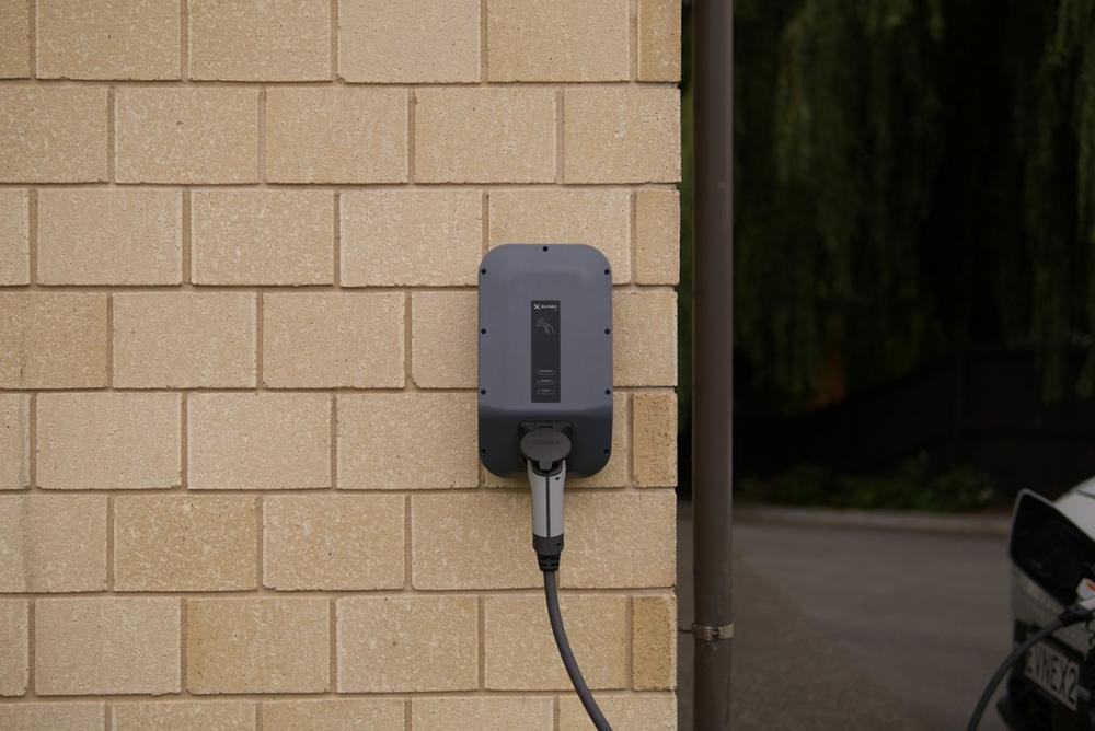 Wall-mounted electric vehicle charger with its cable plugged in, on a light brick exterior wall