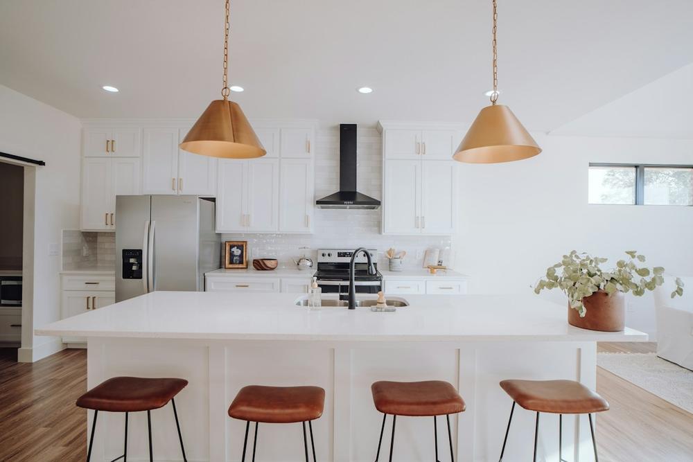 Bright white kitchen with two copper pendant lights over an island with four leather stools