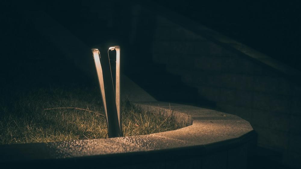 Modern outdoor path light glowing at night beside a curved walkway and grass